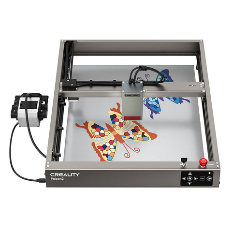 Top view of a CrealityFalcon Falcon2 40W Laser Engraver and Cutter. The machine is crafting two colorful mosaic butterfly designs on a metal sheet. The surrounding frame and mechanical components are visible, with a control box on the left connected by cables.